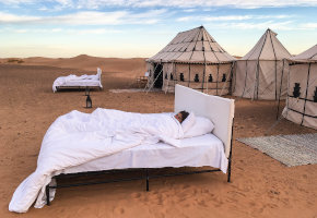 A bed in the middle of the desert with huts around, Sarasota Travel Agent