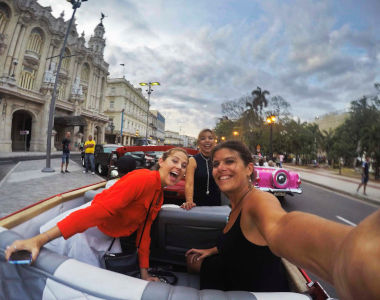 A group of women friends inside a convertible being driven down a main street in Cuba, planned by Sarasota Travel Agent