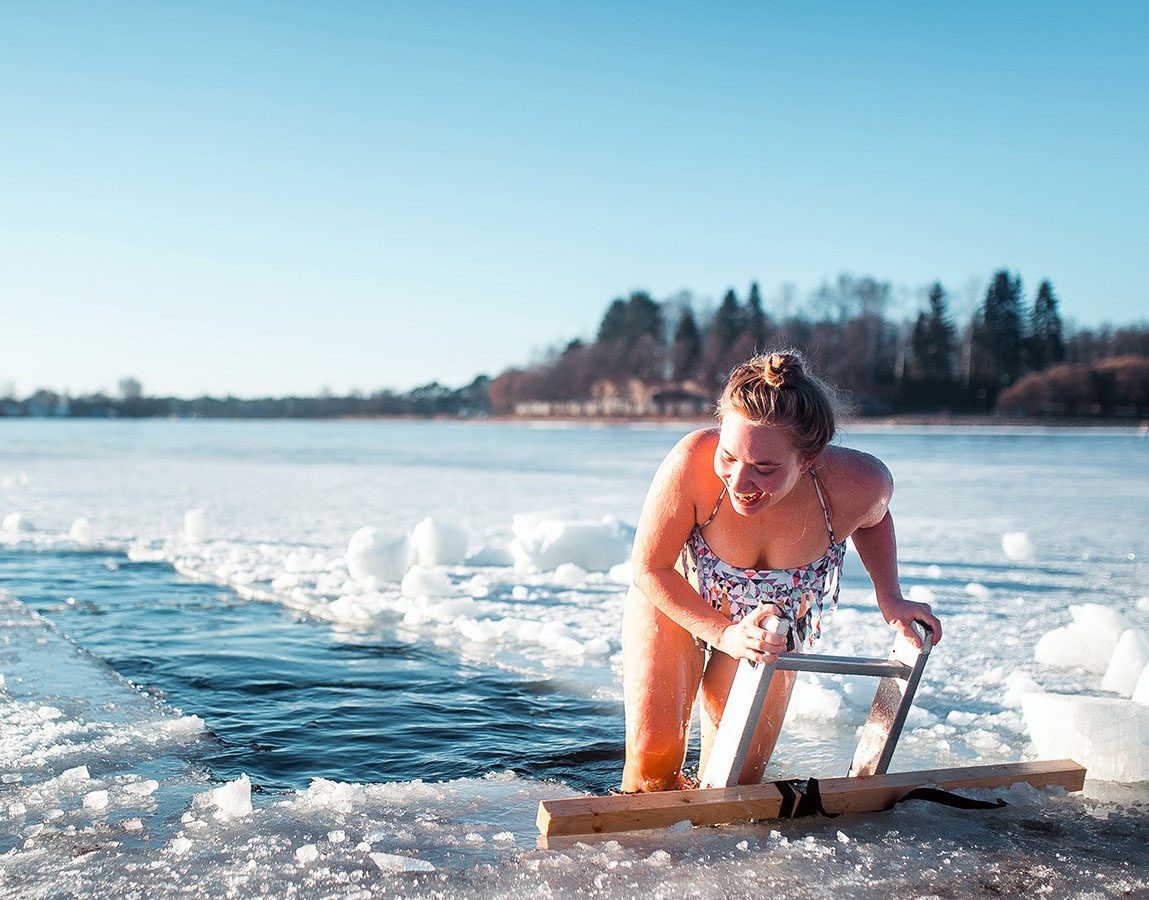 A woman emerging from icy water using a ladder on a cold day.
