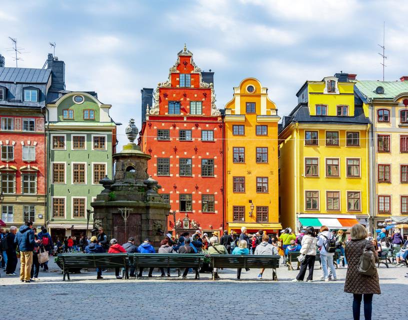 Colorful historic buildings with people gathered in a lively square.