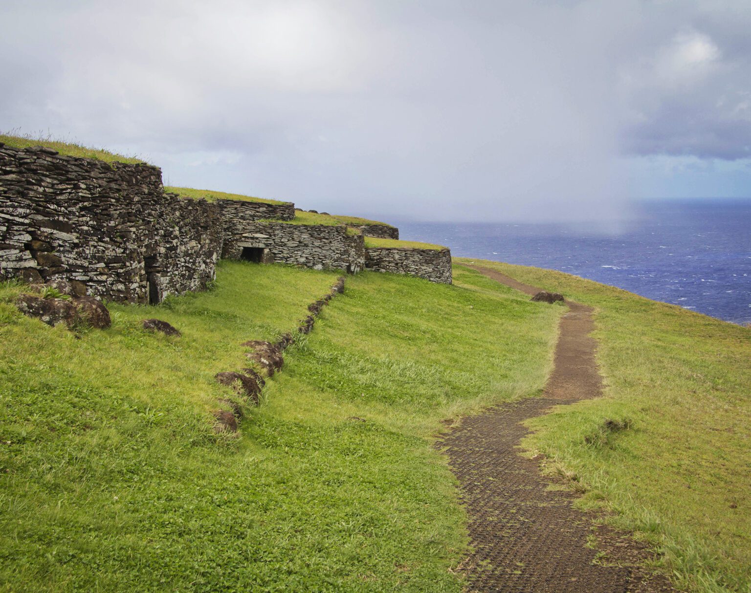 Ancient stone terraces on a grassy hill under a cloudy sky.