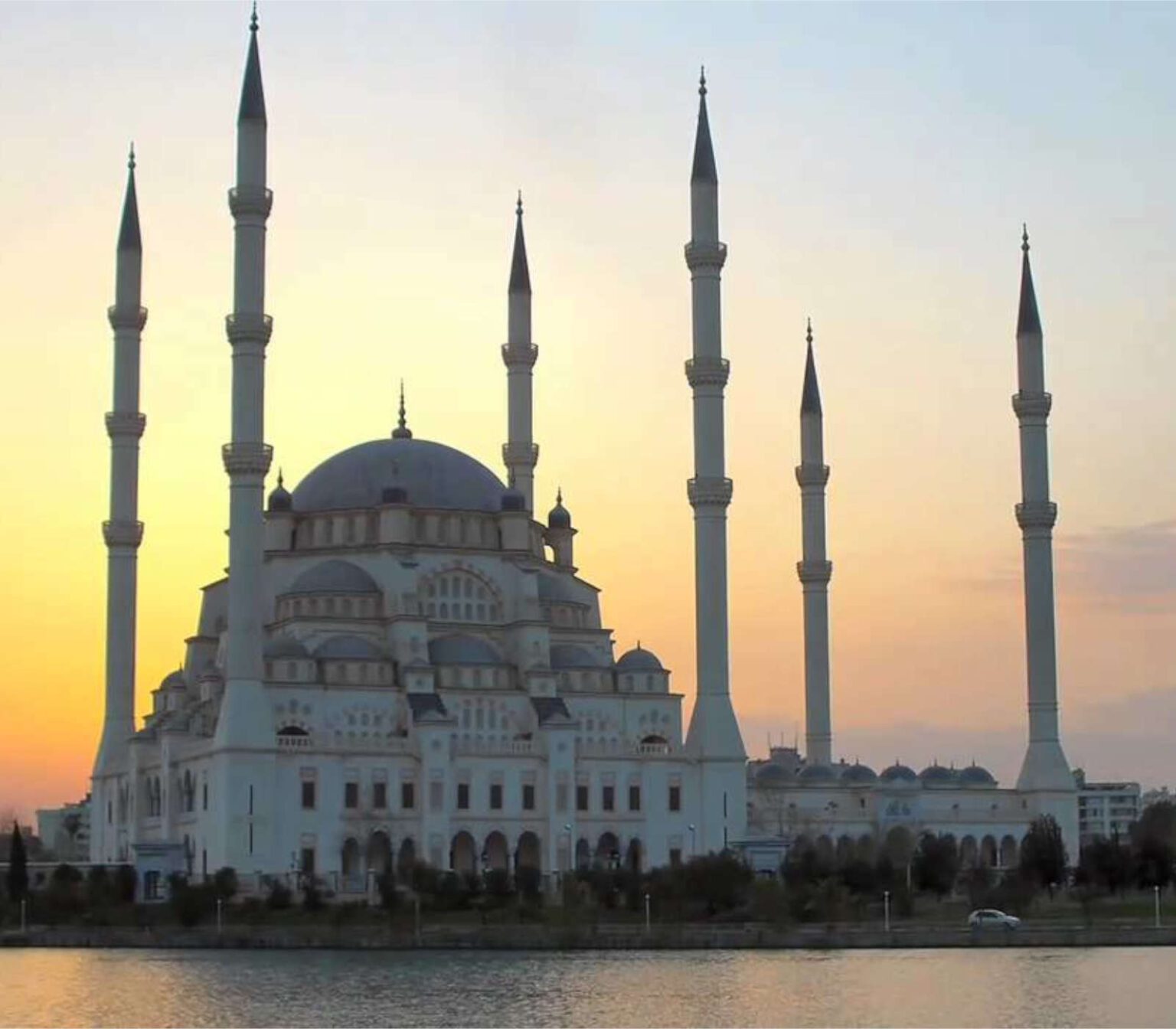 A grand mosque with six minarets at sunset by the water.