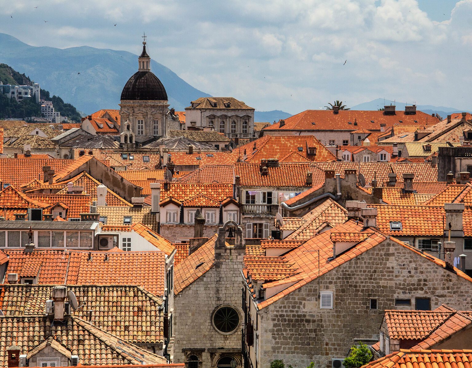 Scenic view of historic city rooftops with terracotta tiles and a domed church tower.