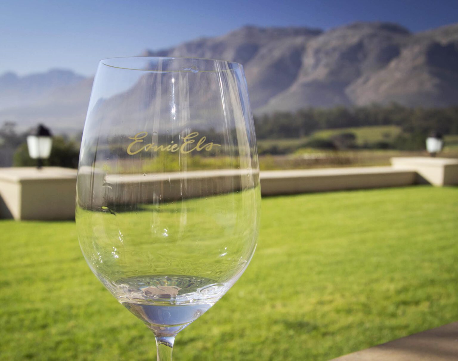 Empty wine glass with vineyard and mountains in the background.