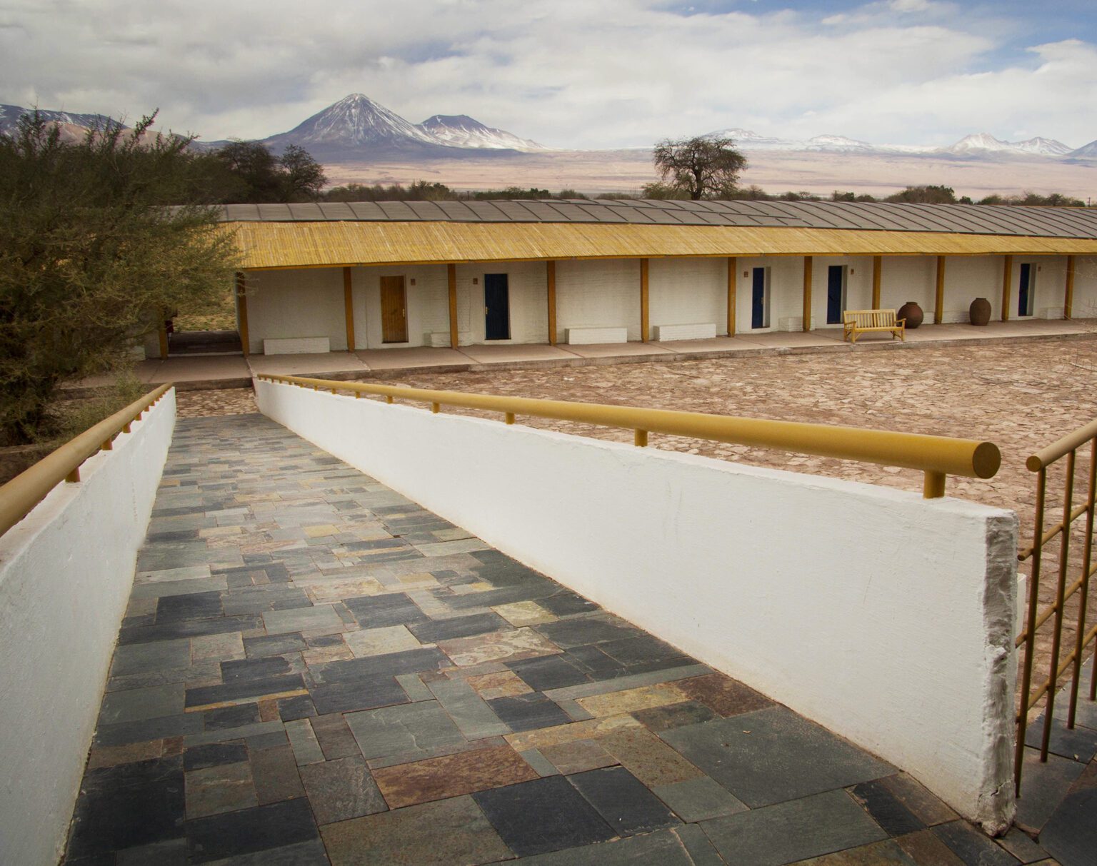 A stone pathway leads to a single-story building with a mountainous backdrop.