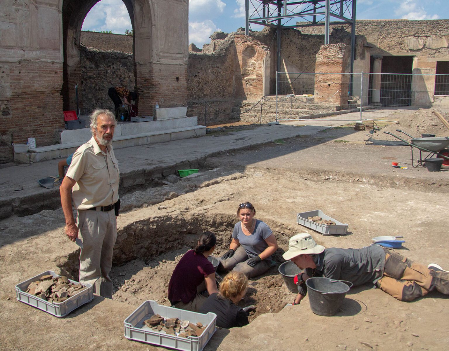 Archaeologists excavate ancient ruins under a sunny sky.