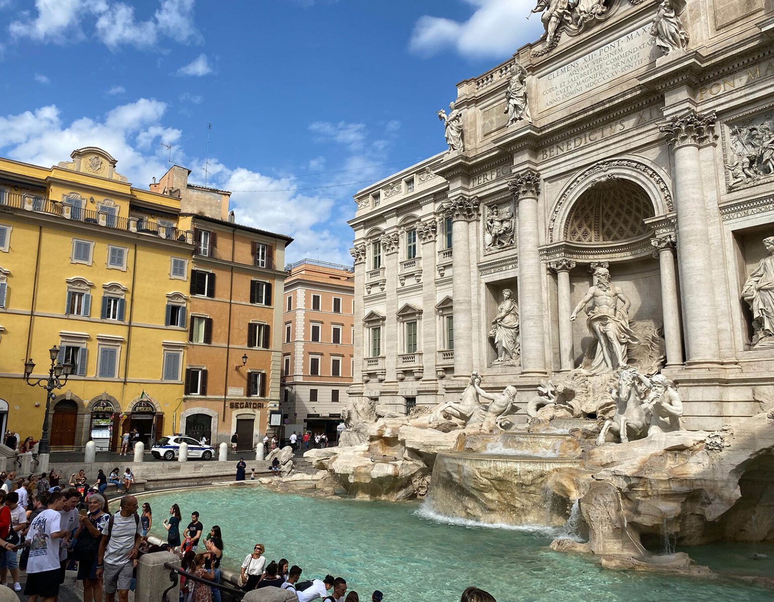 Tourists gather at the iconic Trevi Fountain in Rome on a sunny day.