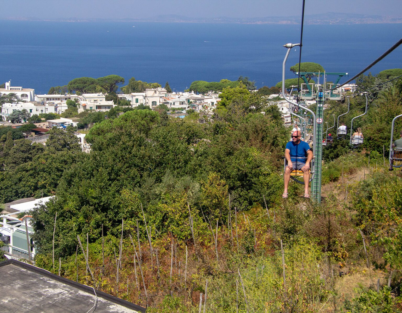 Person riding a zipline over greenery with a sea view.