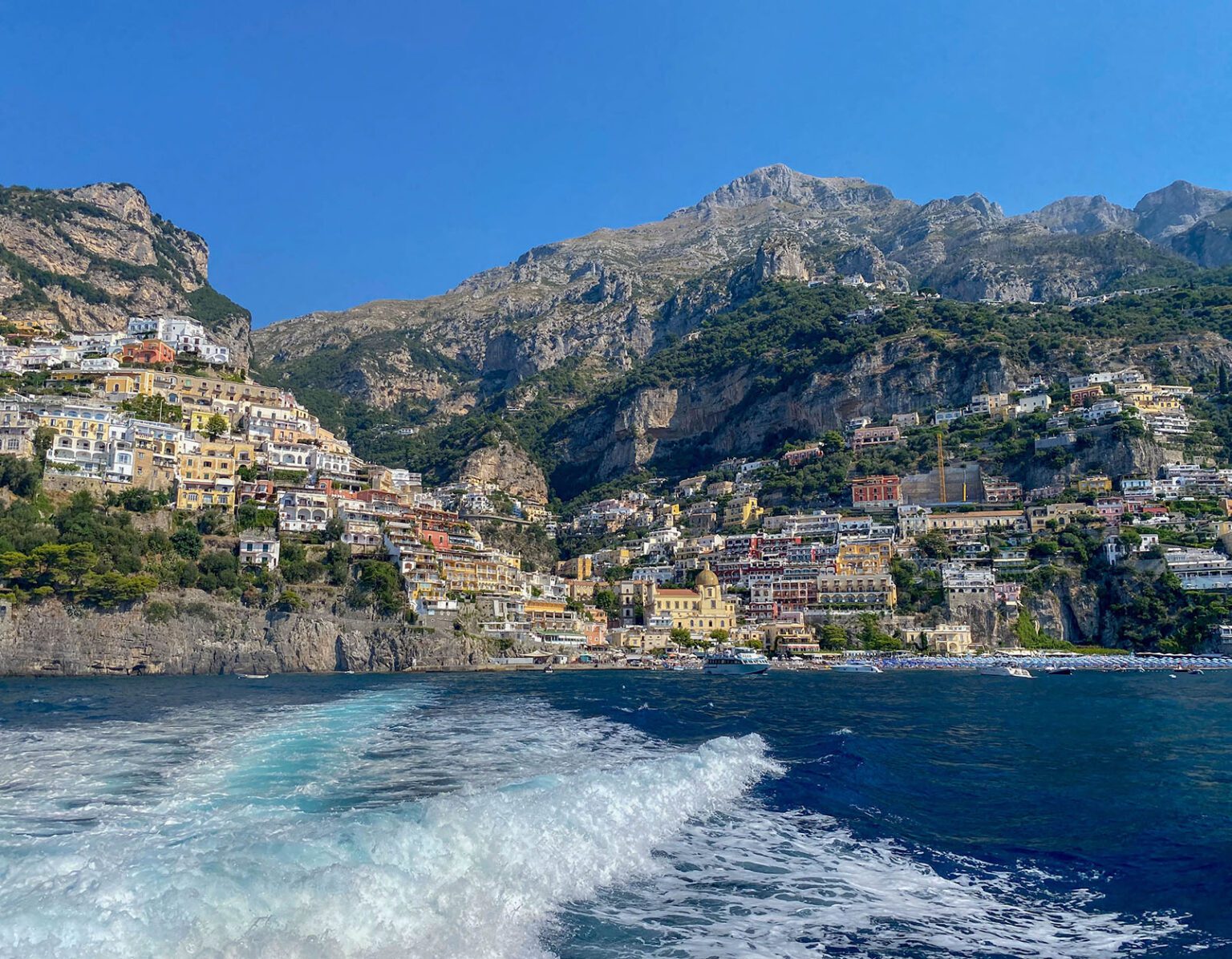 Coastal town nestled against rocky cliffs under a clear blue sky.