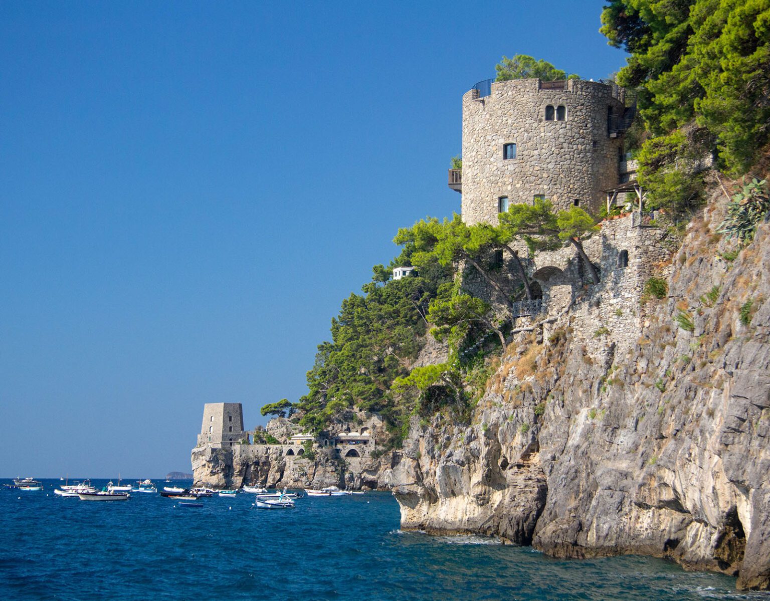 Ancient stone tower on a cliff overlooking the blue sea with boats.