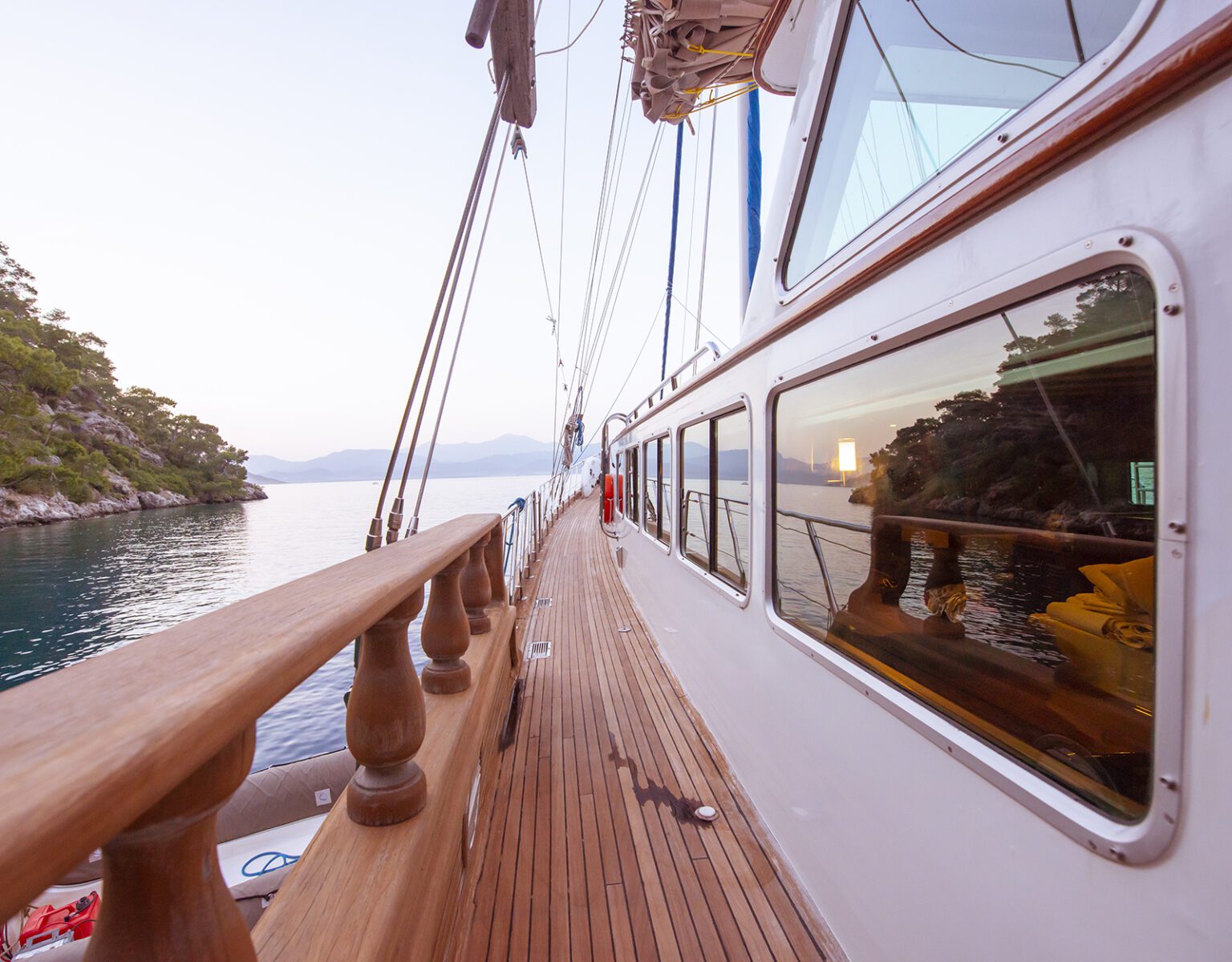 View along the wooden deck of a sailboat at sunset.