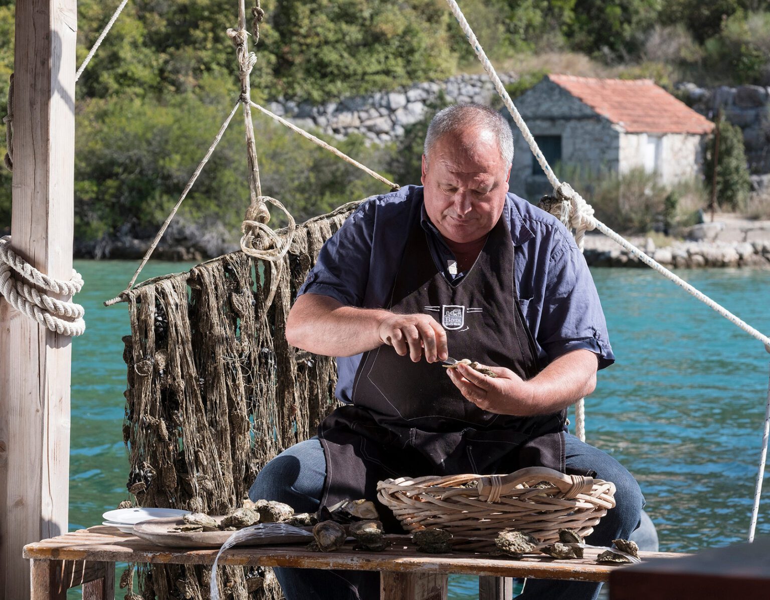A man cleaning oysters by the water.