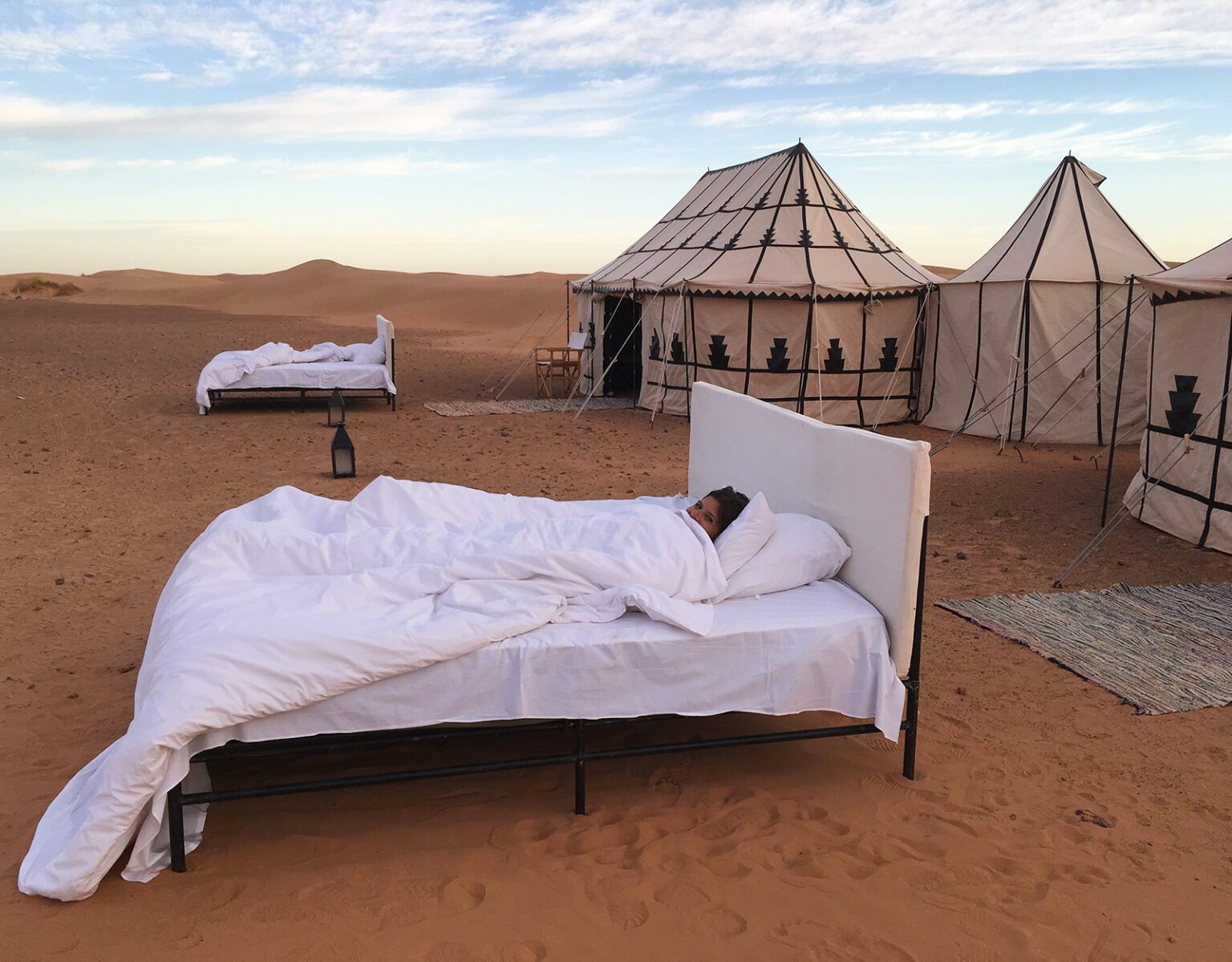 Beds set up in a desert with tents in the background.