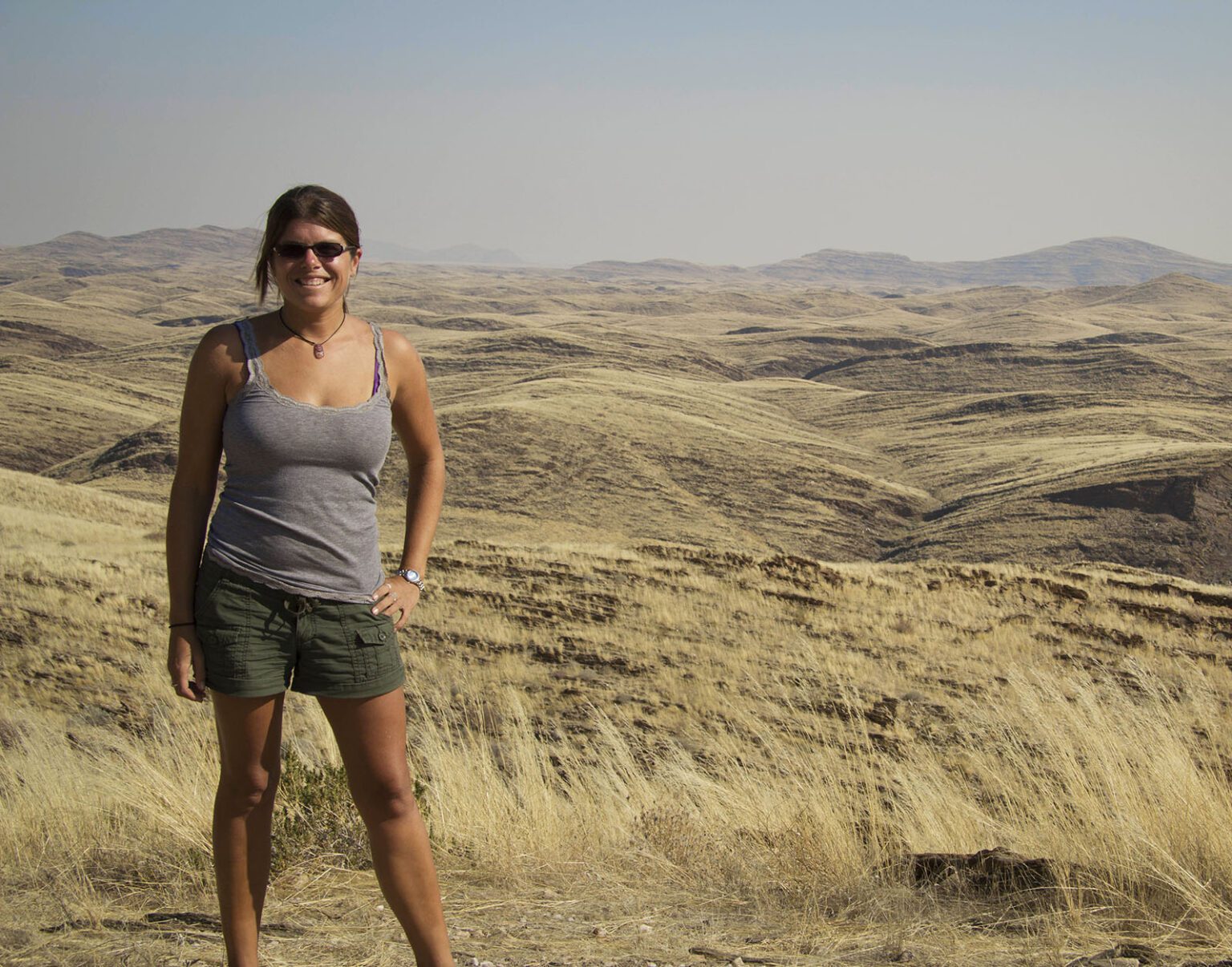 A woman standing on a dry, hilly landscape under a clear sky.