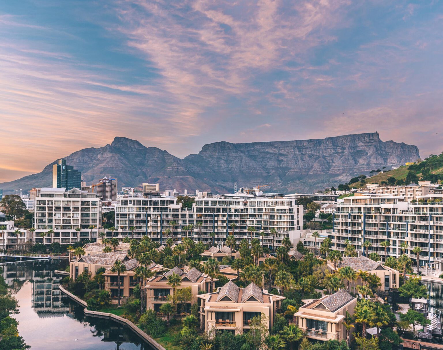 Cityscape with mountains under a colorful sky at sunset.