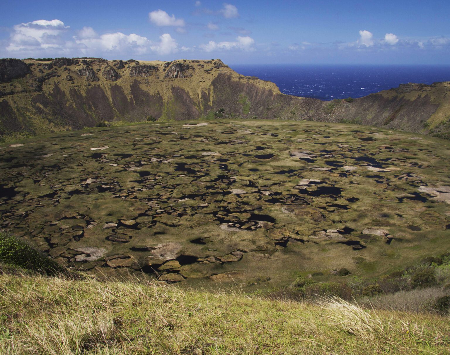Volcanic crater filled with numerous small ponds under a blue sky.