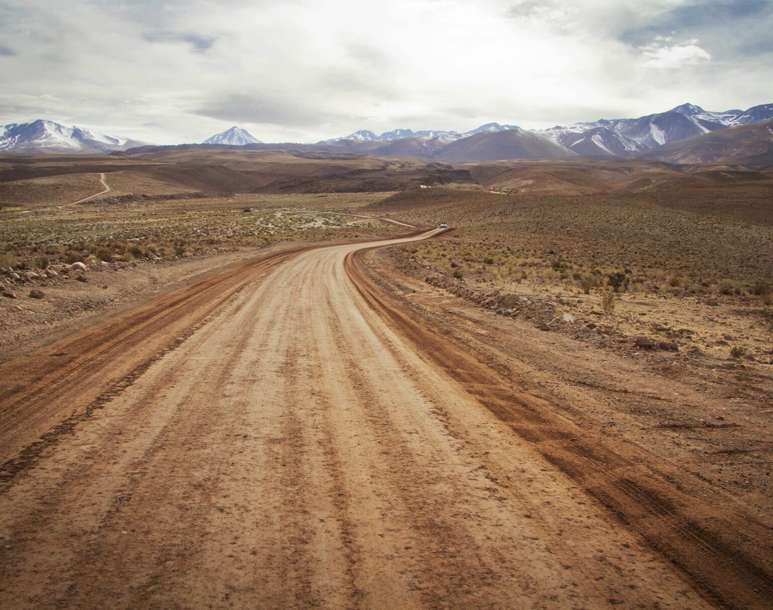 A winding dirt road stretches through a barren landscape towards distant mountains.