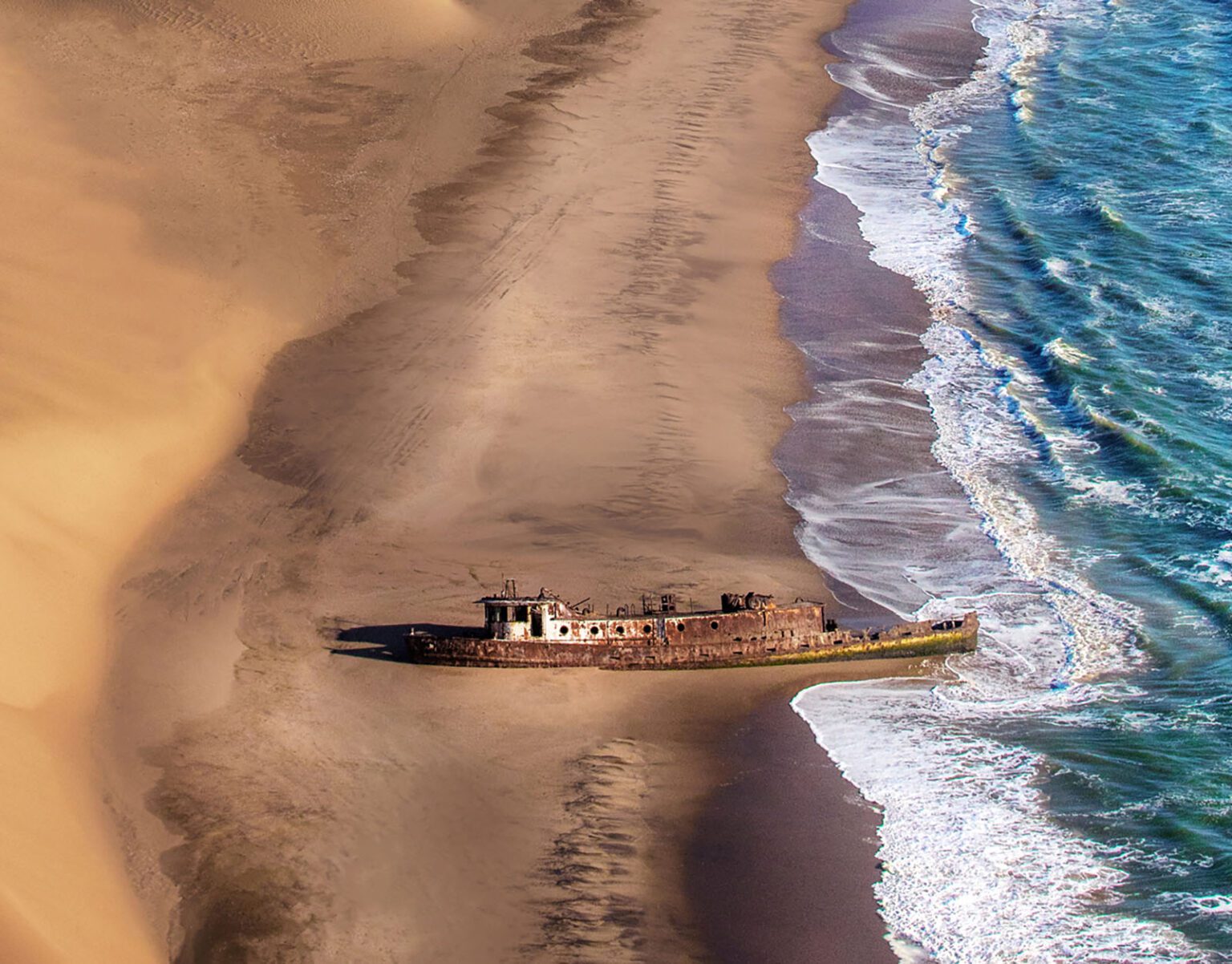 Aerial view of a shipwreck on a sandy beach by the ocean.