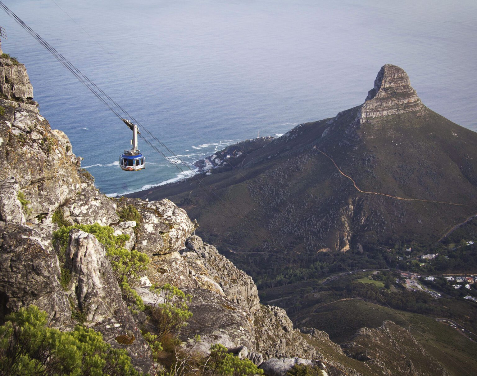 Cable car ascending a mountain with ocean and rugged peaks in the background.
