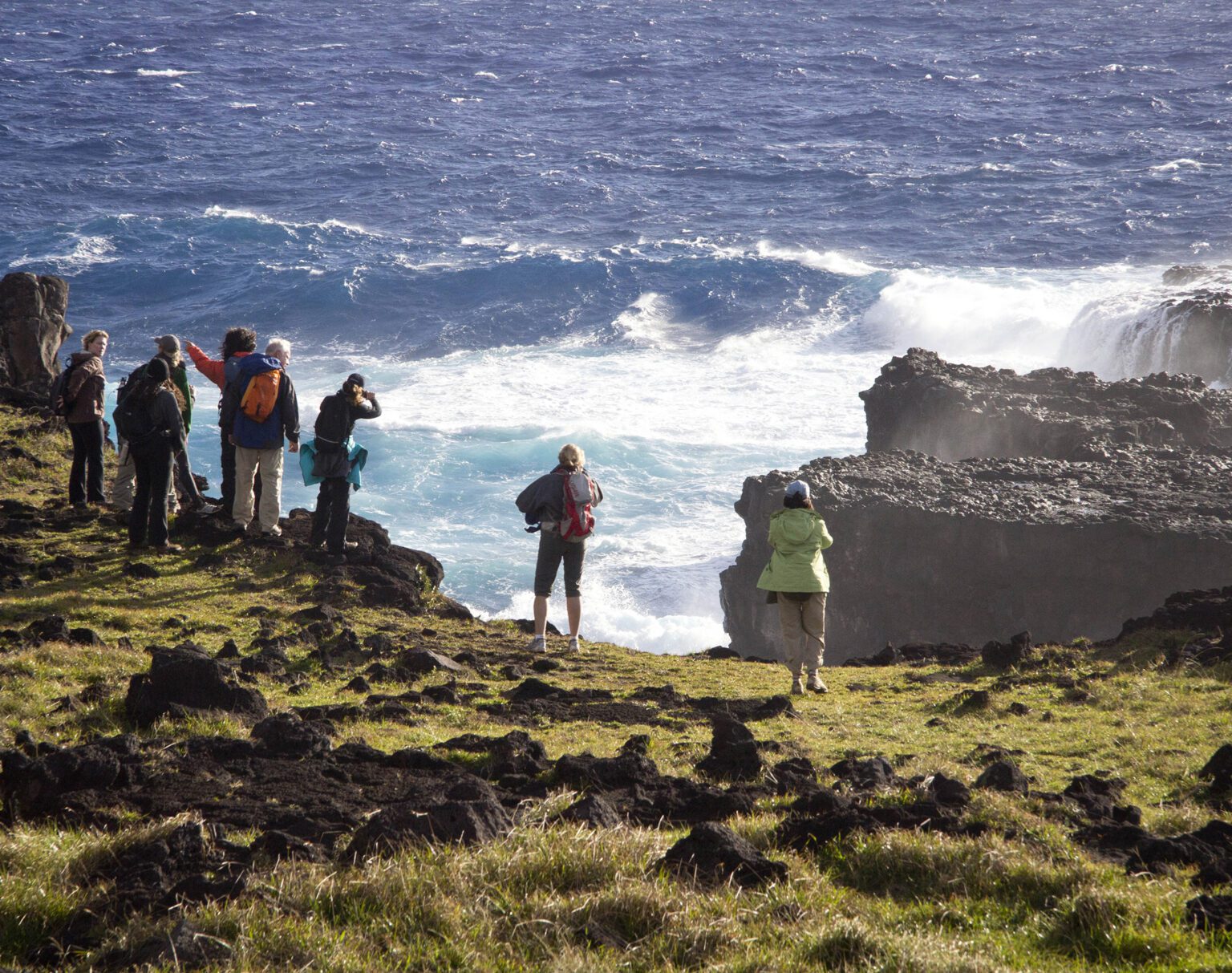 Group of people exploring a rocky coastline with waves crashing.