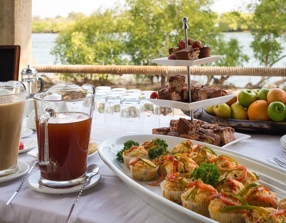 A plate of appetizers, a glass of juice, and a tiered tray with desserts outdoors.