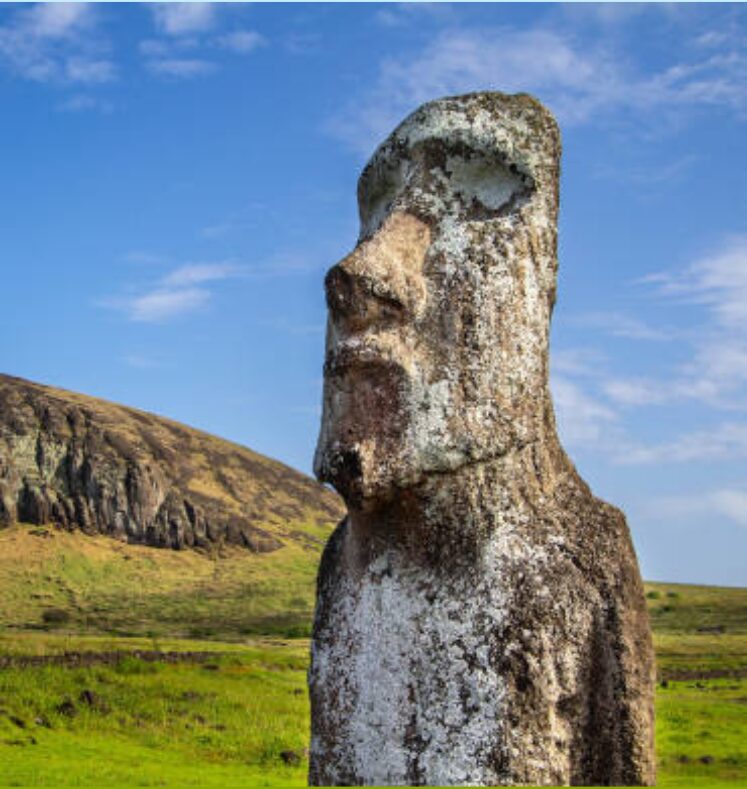 A Moai statue standing on grassy terrain under a blue sky.