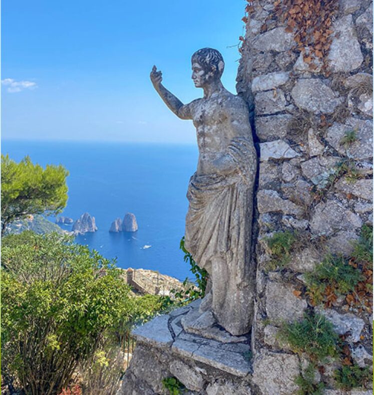 Stone statue overlooking the sea with a sailboat in the background.