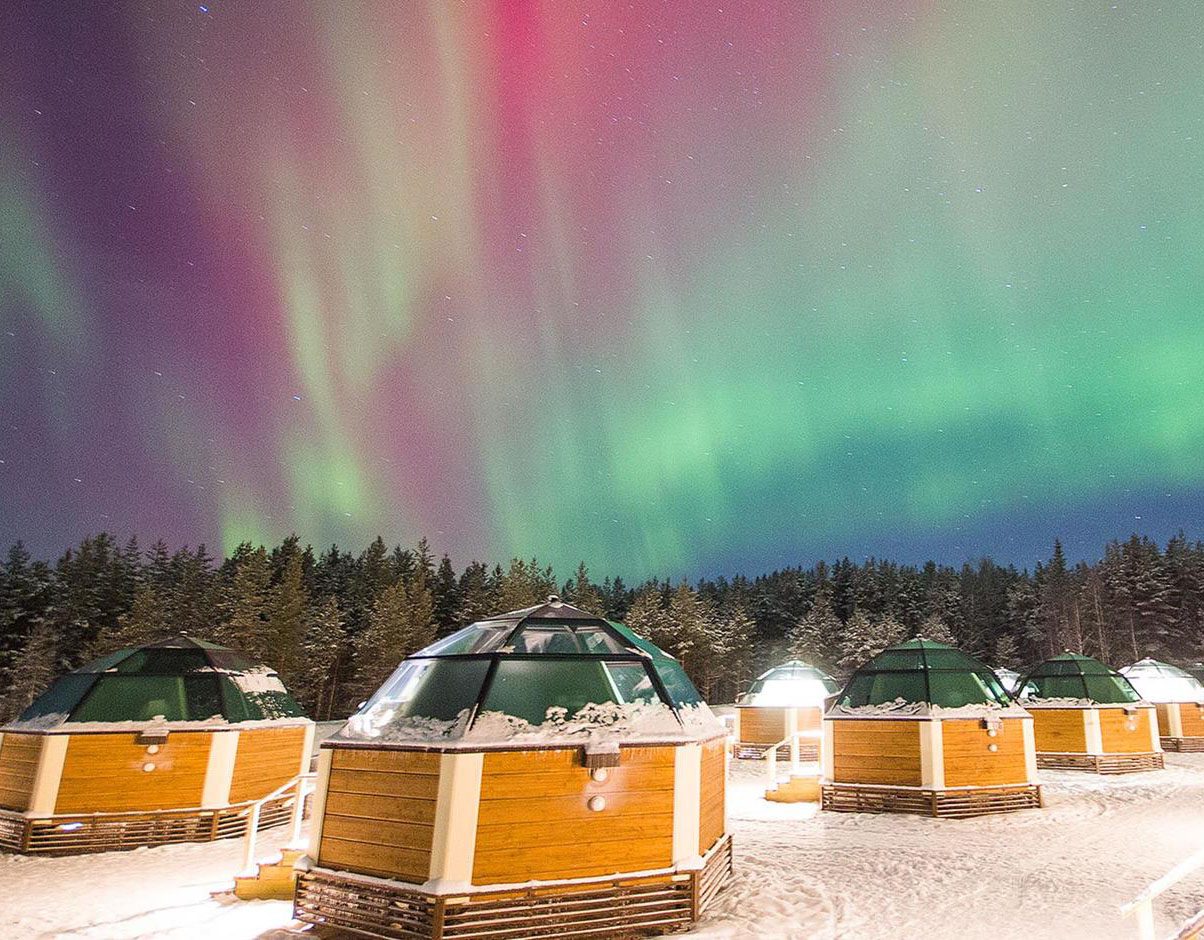 Wooden hot tubs under vibrant northern lights in a snowy forest.