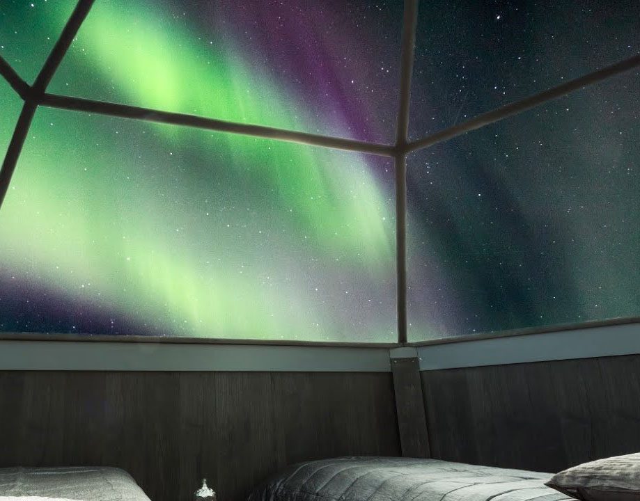 Aurora borealis glowing brightly outside a cozy room with large windows.