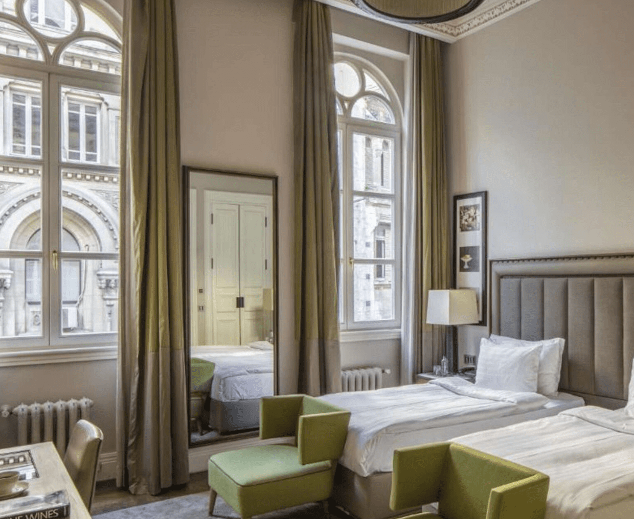 Bright, elegant hotel room with twin beds and tall windows.