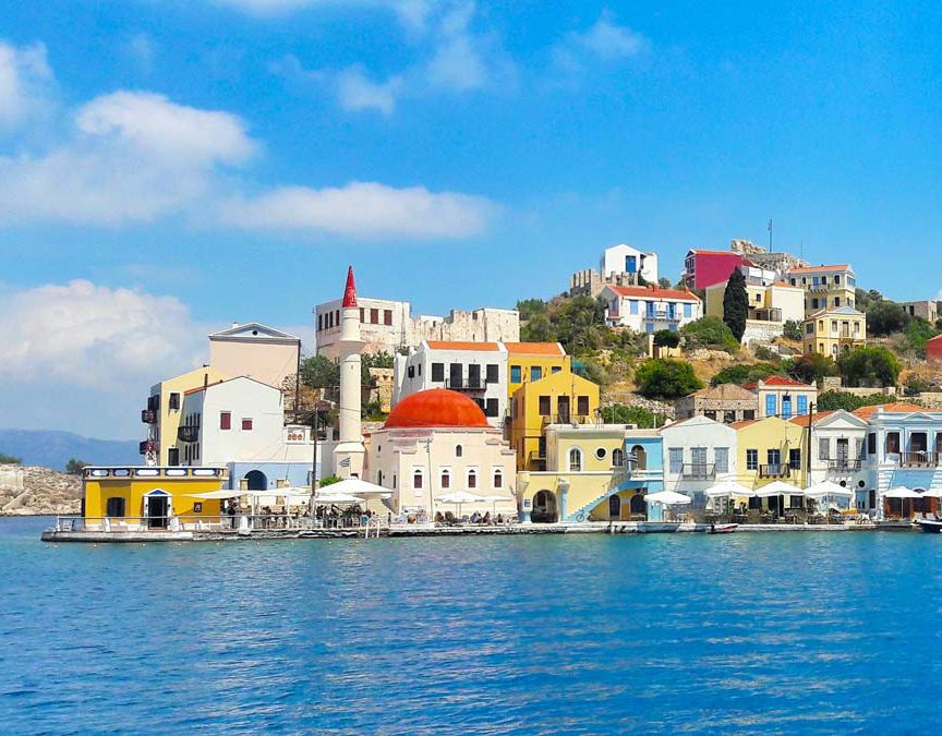 Colorful coastal village with clear blue waters and traditional buildings under a bright sky.