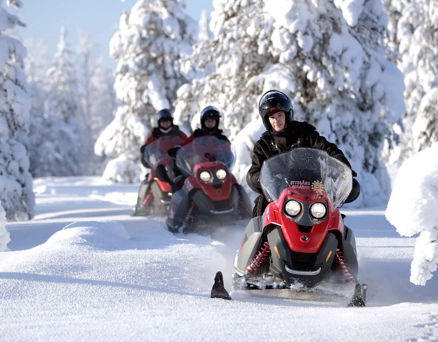 People riding snowmobiles through a snowy forest.
