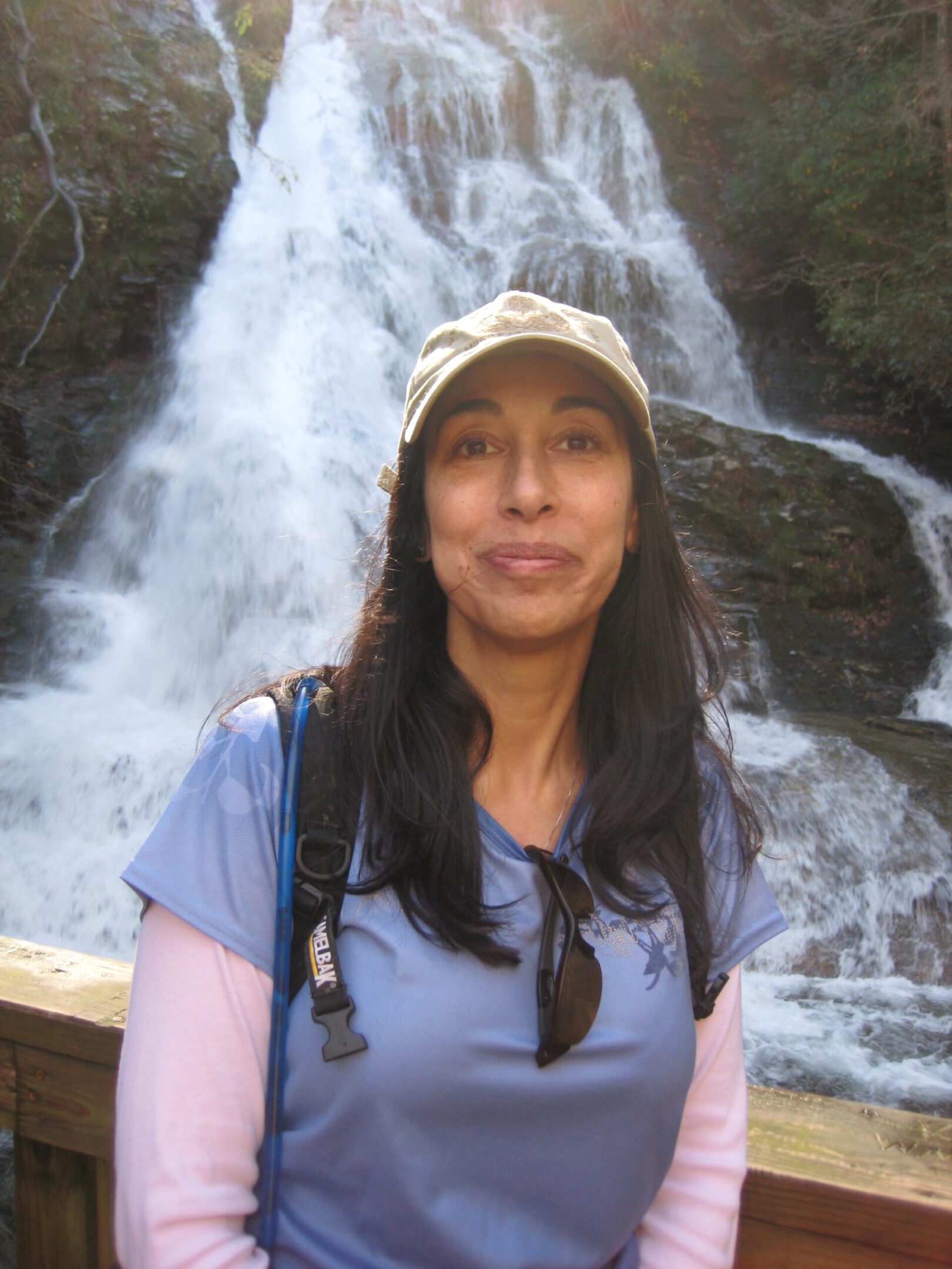 Woman in a cap standing in front of a waterfall.