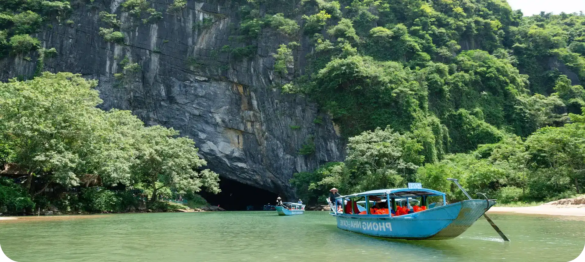 Tourists in boats exploring a lush riverside cave.