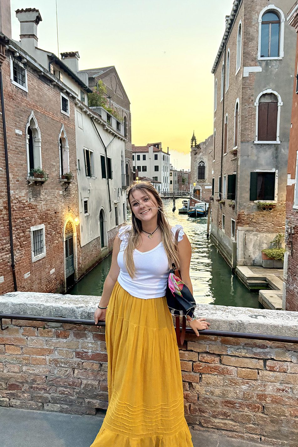 A woman smiling on a Venice canal bridge at sunset.