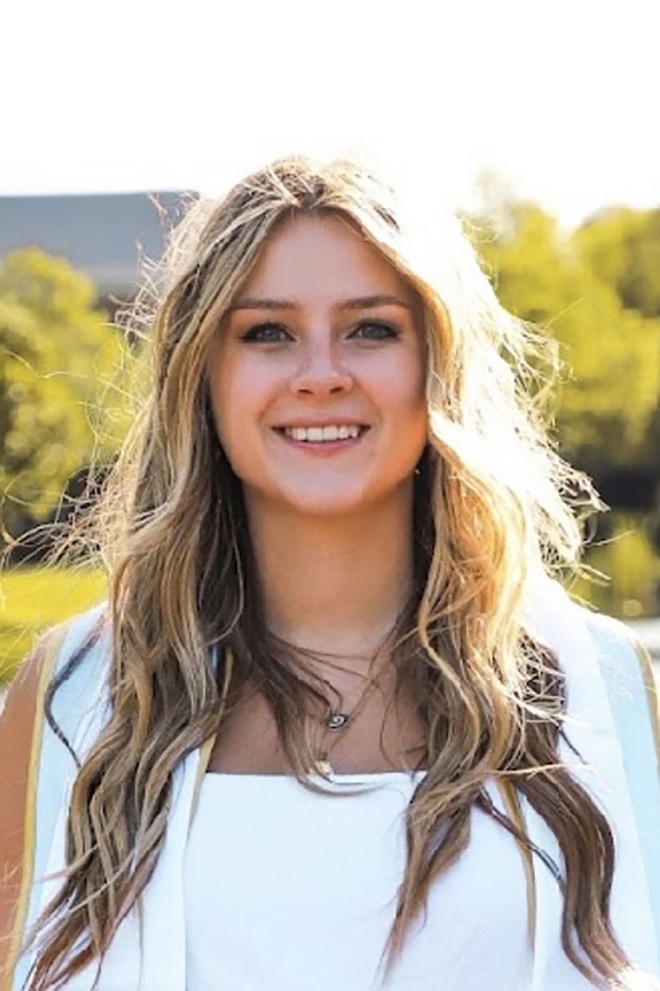 Smiling young woman outdoors with sunlight and greenery.
