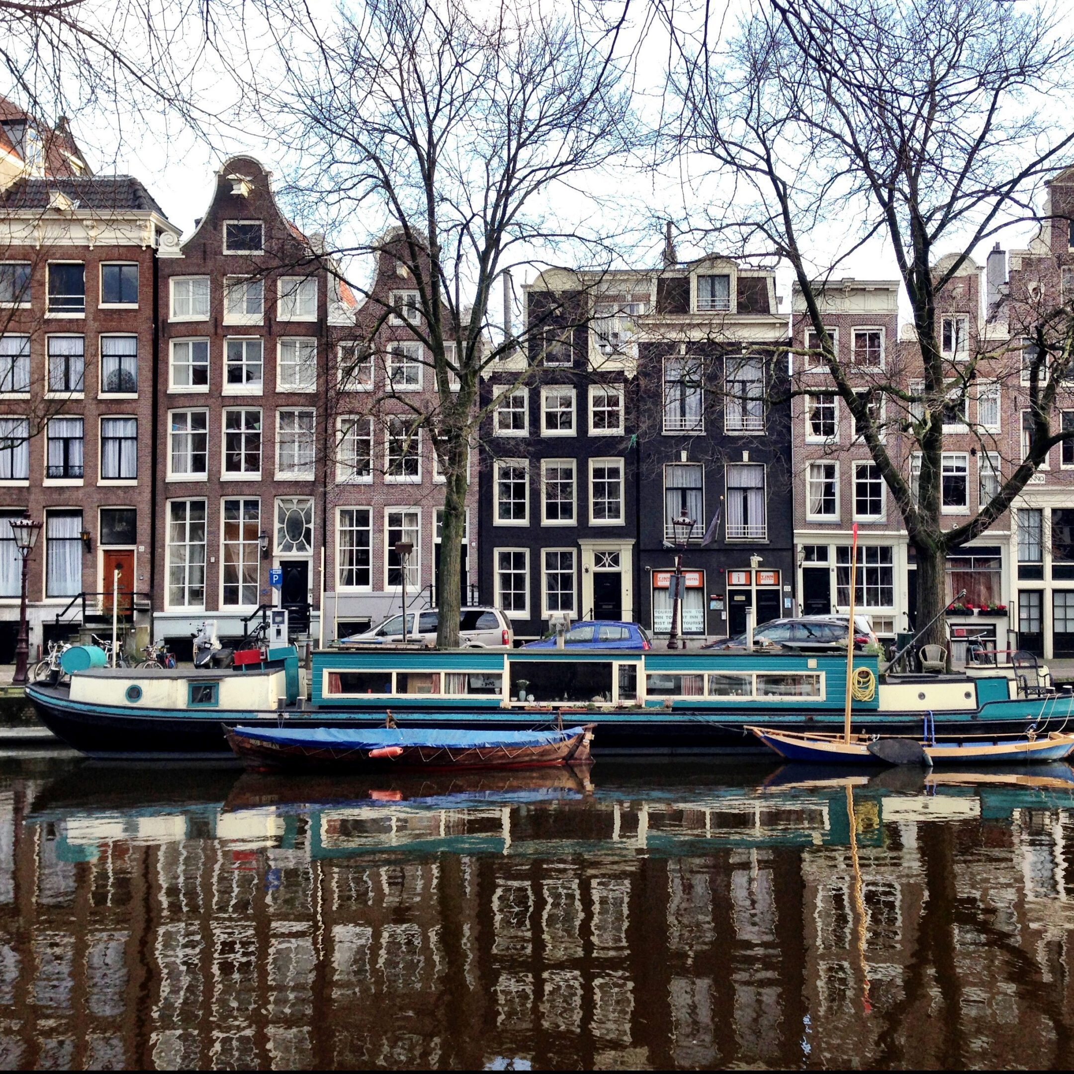 Boats docked along a canal with traditional Dutch houses and leafless trees.