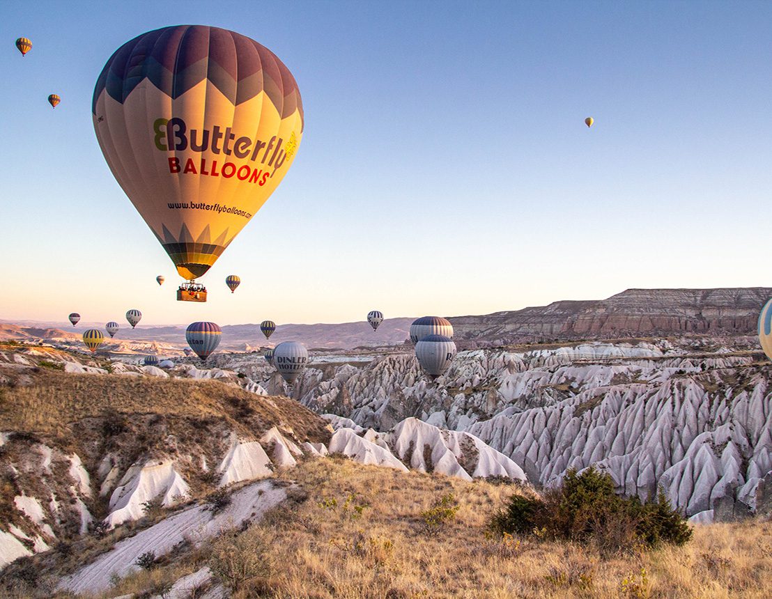 Hot air balloons soar over a rocky landscape at sunrise.