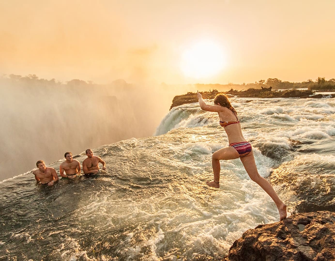 Woman jumping into water at sunset.