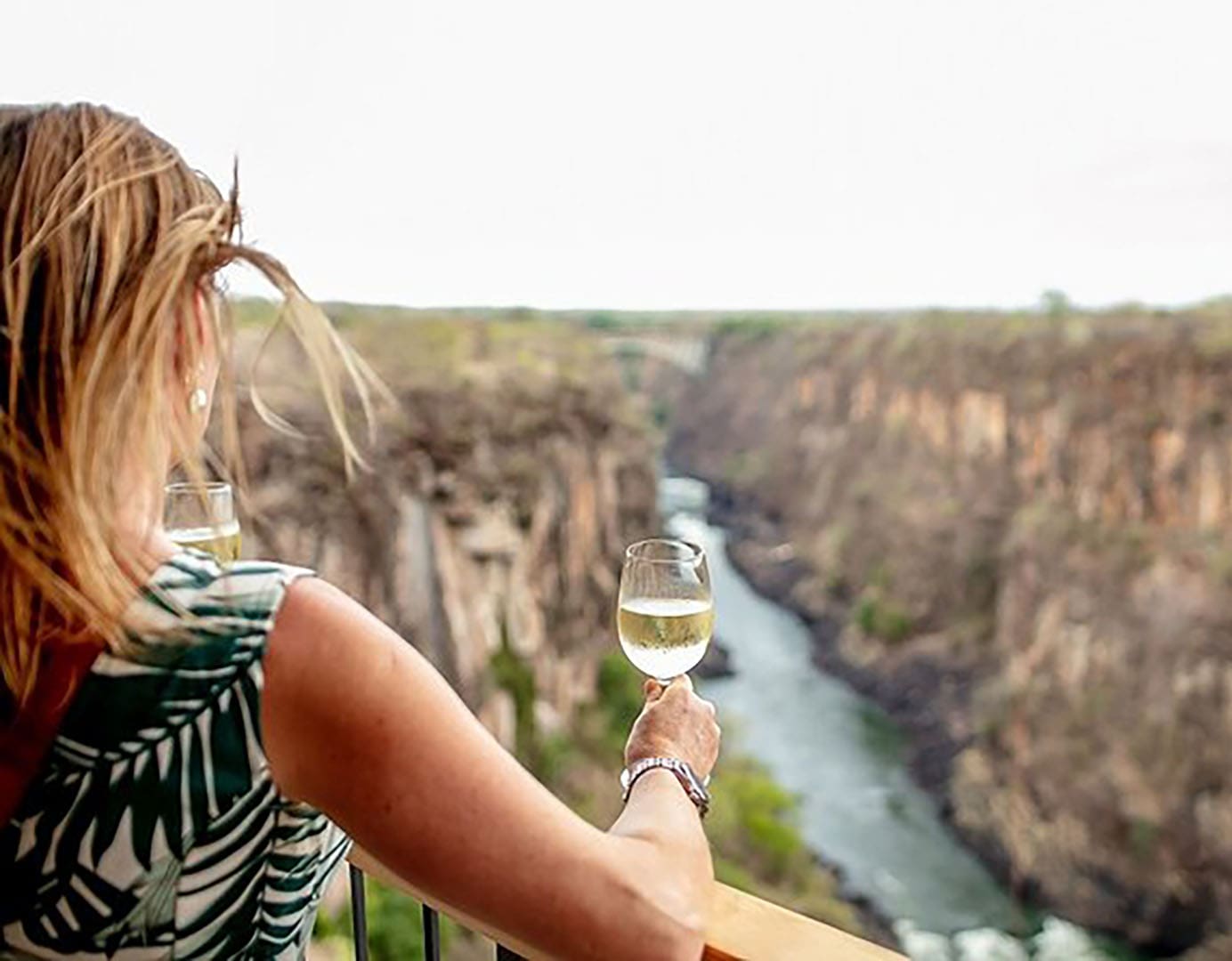 Woman enjoying wine by a scenic canyon.