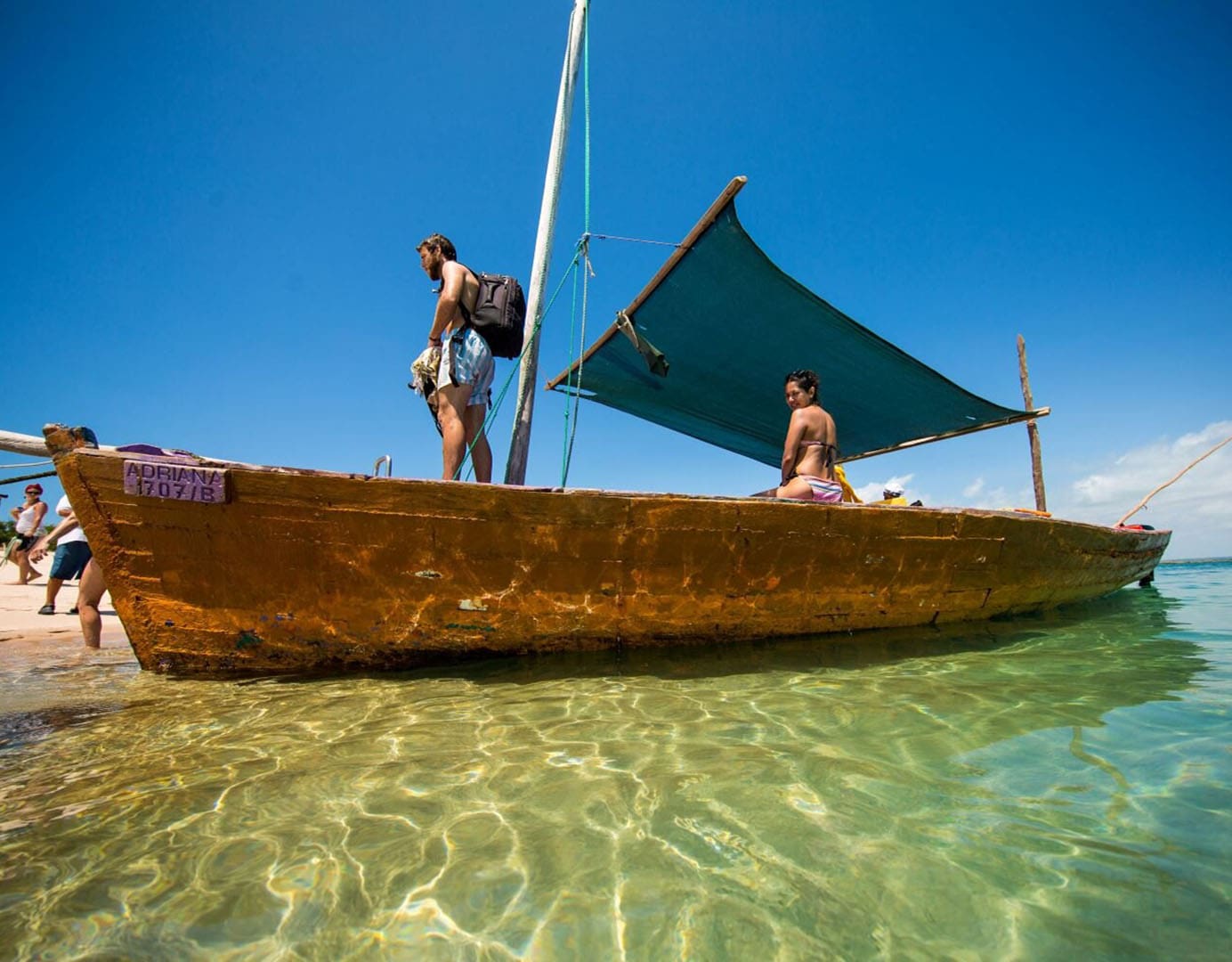 Two people on a wooden boat in clear water.